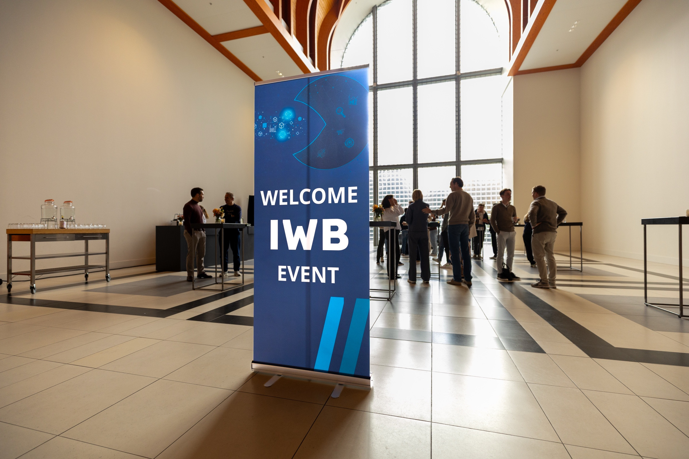 De welkomstbanner van een IWB-event met gasten in de zaal